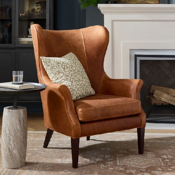 Brown leather wingback chair by a fireplace